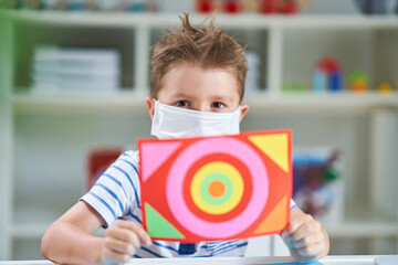 Adorable little boy in kindergarten with mask on due to coronavirus pandemic
