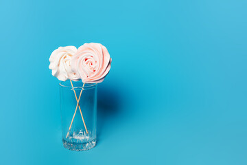 Beautiful tender meringue on a stick in a glass on a blue background, March 8, Mom day, birthday present, sweets