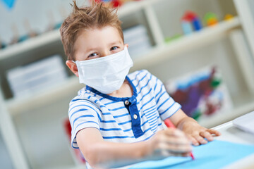 Adorable little boy in kindergarten with mask on due to coronavirus pandemic