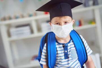 Fototapeta na wymiar Adorable little boy in kindergarten with mask on due to coronavirus pandemic