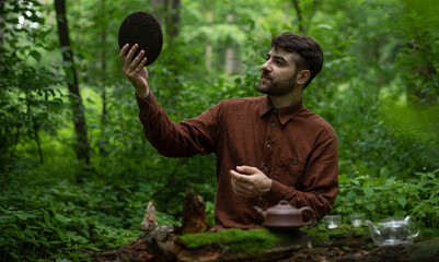 Naklejka na ściany i meble Young man holding round flat disk of shu puer tea in summer forest 