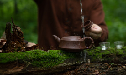 Man pouring water in clay teapot during tea ceremony in forest