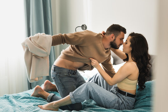 side view of passionate man holding sweatshirt of attractive girlfriend in bedroom
