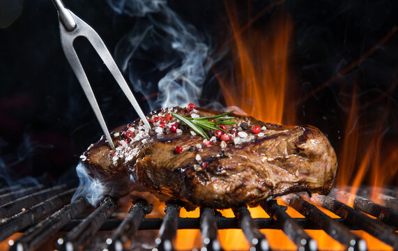 Tasty beef steak on cast iron grate with fire flames. Freeze motion barbecue concept.