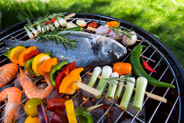 Grilled sea fishes with vegetable, skewers and prawns on a barbecue grill, top view.