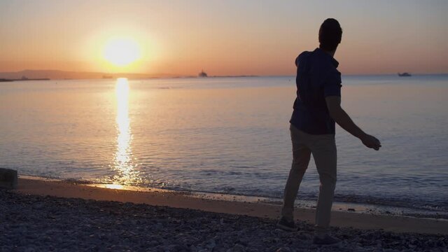 Young man relaxing on beach and throwing pebbles in sea