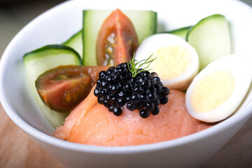 Summer salad with salmon and black caviar, on a rustic wooden table