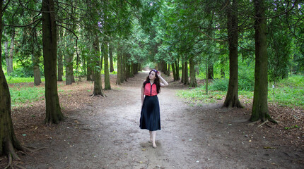 Young girl in sunglasses stands on the path between the rows of fir trees.