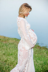 Fototapeta premium portrait of young blonde pregnant woman in white dress which is standing near lake like swan. pregnancy concept, free space