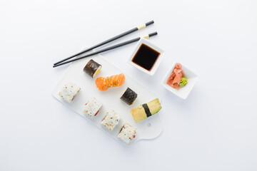High angle view of sushi rolls and nigiri meal set with chopsticks, soy sauce, wasabi and gari on table.