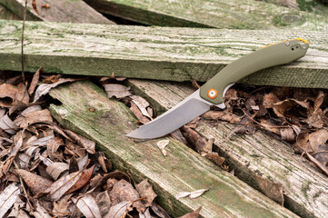Knife with a green handle on green wooden boards. Photo of a knife in the forest.