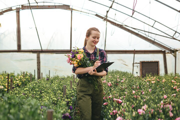 Gardener woman working on flowers in greenhouse  and makes notes. Floral business concept.