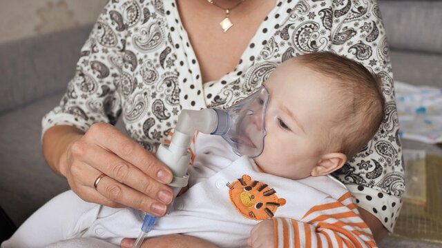 Infant getting breathing treatment from mother while suffering from illness.