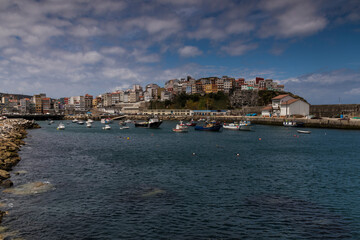 Obraz premium Fishing boats moored in the port of Malpica de Bergantiños under a blue sky and stratus clouds
