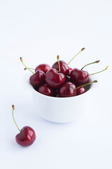 Obraz na płótnie Canvas Red cherries in the white bowl on the white background. Location vertical. Copy space.