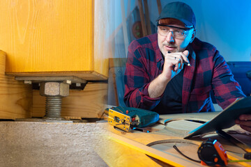 A man in a black cap in a carpenter's shop. A carpenter is working on a drawing of a set of...