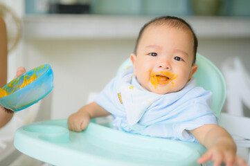 Asian 7 months baby boy eating blend food on a high chair, Mother  feeds a Little Baby with a Spoonful of food.