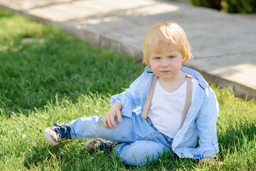 Little blond boy sits on the green grass.
