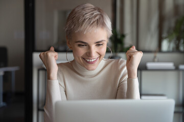 Happy woman employee sitting at workplace look at laptop screen feels excited received great...