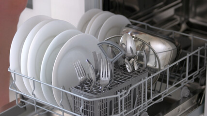 Close up open dishwasher with clean plates and cutlery. Modern technology for housewife. How to...