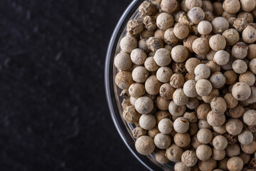white peppercorns in glass bowl on stone background