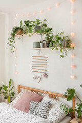 Spathiphyllum, ivy, pothos, alocasia and other plants in the bedroom for the air cleaning and better sleeping, interior plant next to the bed with small cute lighting chain