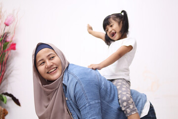 Asian muslim mother playing with her little baby girl daughter sit on her back, acting like a horse for her kid, happy smiling