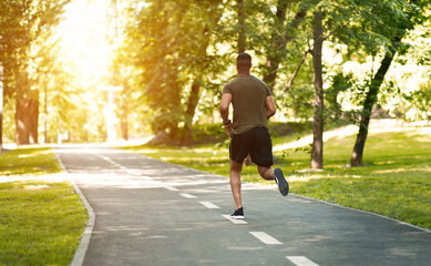 Back view of millennial sprinter on his morning run at park on sunny morning, empty space