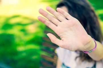 Beautiful young girl sitting in a park and hiding face with hand