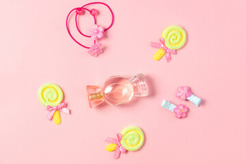 Children's flat lay. Perfume in the form of candy, children's jewelry and hair accessories on a pink background. Accessories for little girls.
