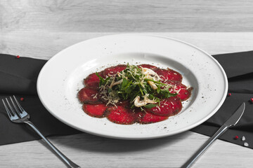 Close up of beef carpaccio in on the white plate with arugula, mushrooms, Parmesan cheese, seasoned with sea salt with rosemary, thyme and garlic on the woodenbackground.