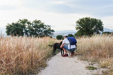 Crouched man with a backpack caressing his labrador retriever in the field at sunset