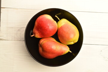 Sweet juicy pears in a black ceramic plate on a white wooden table.