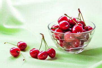 Juicy ripe sweet cherries in glass bowl on gently green cloth background