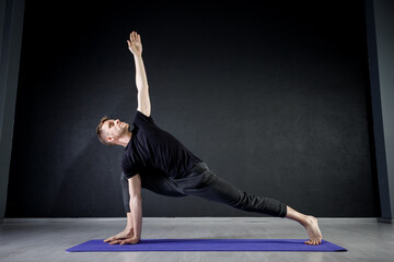 Young man doing leg stretching exercises on a yoga mat in the gym. Practising yoga positions.