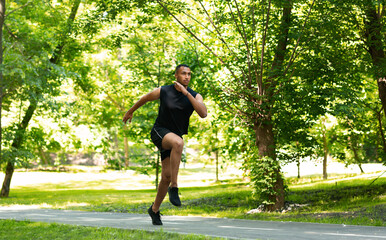 Handsome millennial sprinter running on track at beautiful park, copy space