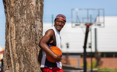 Black basketball player holding ball near outdoor sports arena, free space