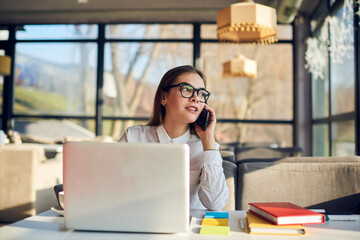 Portrait of attractive young female freelancer providing online marketing services promoting products of company on websites and social networks working in free time in cafe having phone conversation