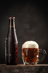 Bottle and jug of beer on  wooden base on dark background. Vertical format.