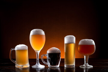Variety of beers in different glasses on wooden base. Dark and orange background.