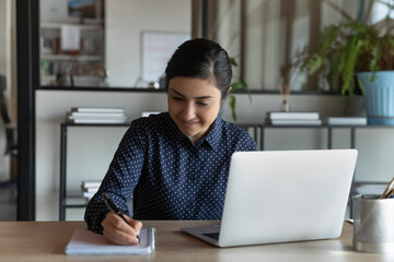 Indian girl sit at table make notes on notepad preparing for college exam get information from internet prepare thesis. Businesswoman improve language knowledge use pc do task, self-education concept