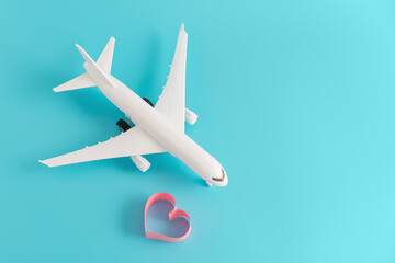 Love travel concept. Miniature plane with heart shaped symbol on bright blue background. Vacation and romance.