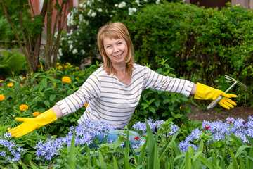 Happy mature woman with garden tool working in her garden on a flower bed. A smiling woman, 59...