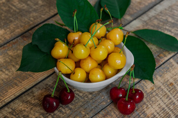 Red and yellow cherries. Contrast of colors. Fresh ripe sweet cherries in a white plate on a wooden background. Close-up
