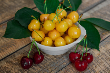 Red and yellow cherries. Contrast of colors. Fresh ripe sweet cherries in a white plate on a wooden background. Close-up