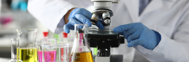 Close-up of researcher in protective glasses and gloves. Lab assistant making analysing sample of experiment in microscope. Chemical experiments concept