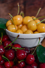 White plate with ripe yellow and red cherries. Fresh sweet cherry with leaves and drops of water. Closeup of fresh ripe sweet yellow and red cherries. Wood background