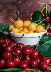 White plate with ripe yellow and red cherries. Fresh sweet cherry with leaves and drops of water. Closeup of fresh ripe sweet yellow and red cherries. Wood background