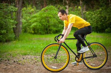 Obraz premium Portrait of a young man moving on a Bicycle. In a public Park, among trees and vegetation.