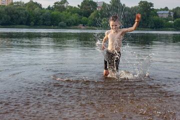 a boy splashes water in the river. bathes. children's happiness